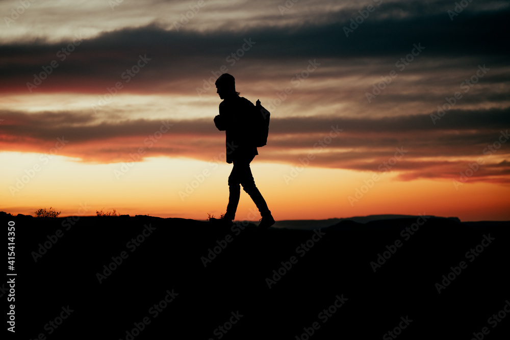 Silhouette male adventurer hiking during sunset on mountain top