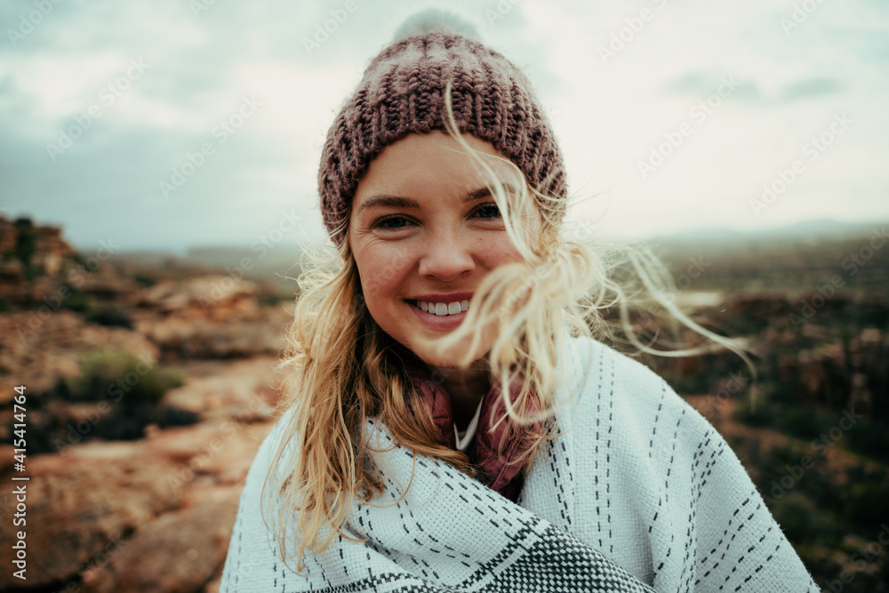 Caucasian female smiling wearing beanie wrapped in cozy blanket enjoying camping on mountain top Caucasian female smiling wearing beanie wrapped in cozy blanket enjoying camping on mountain top
