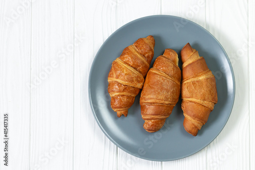 Plate of freshly baked croissants on white wooden table top view