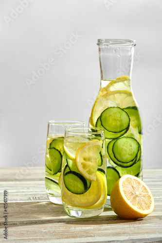 Sassi water with lemon and cucumber in a bottle and glasses on a light wooden background in a high key