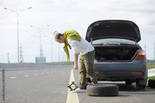Replacing the wheel of a car on the road. A man doing tire work on the sidelines.