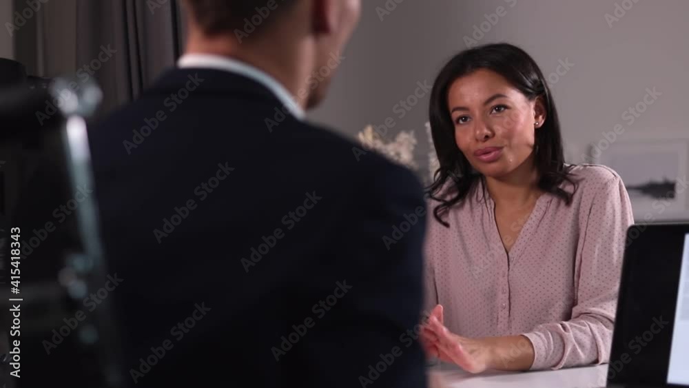 Man and woman talking and sitting at table during meeting in modern office spbi. Male professional interviews female candidate and looks at paper resume, sits at desk with laptop in light room Man and woman talking and sitting at table during meeting in modern office spbi. Male professional interviews female candidate and looks at paper resume, sits at desk with laptop in light room