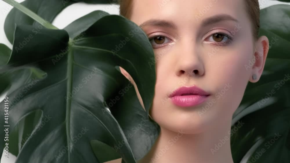Closeup face of young beautiful woman with a healthy clean skin. Beautiful white girl with big green leaves. Beauty and spa treatment concept. Pretty woman with natural makeup and plant near face. Closeup face of young beautiful woman with a healthy clean skin. Beautiful white girl with big green leaves. Beauty and spa treatment concept. Pretty woman with natural makeup and plant near face.