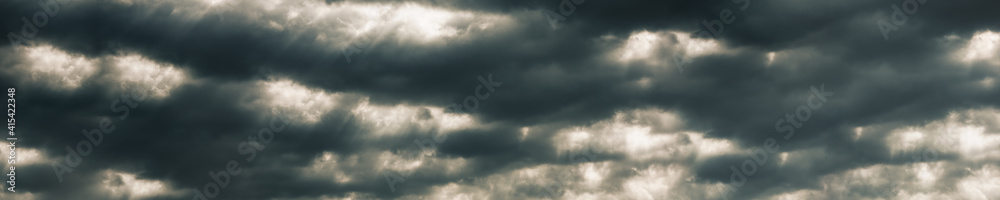 panorama dramatic sun rays through a cloudy dark sky 