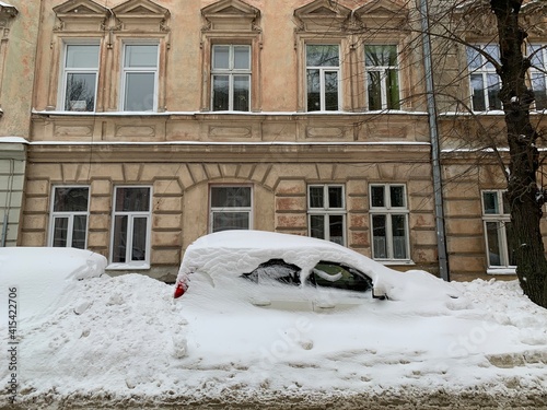 The car was covered with snow in the parking lot. Cars under a large layer of snow. Snowfall on the streets of Europe.