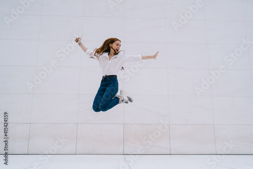 Excited hipster girl in casual apparel feeling satisfied happiness and freedom while jumping near promotional background with copy space area for fashion advertising, emotional female youngster