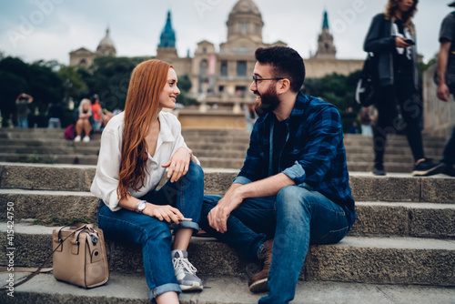 Happy couple in love resting at street stairs in historic center and discussing getaway vacations, smiling hipster guys enjoying positive relationship and time for together international travelling