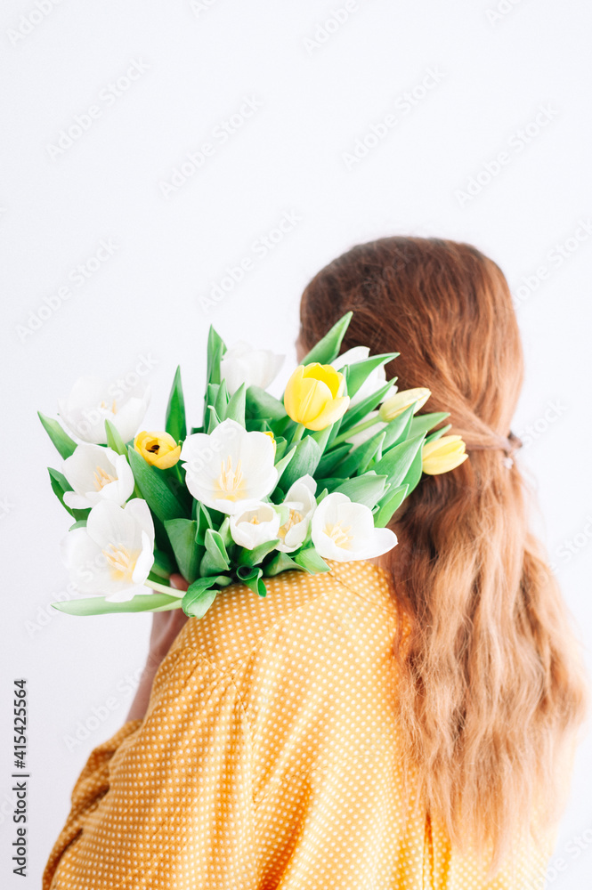 Naklejka premium Back view of redhead woman with Yellow and white tulip bouquet on her shoulder.