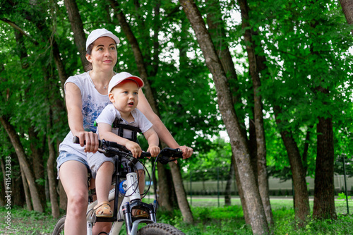 mother and son ride a Bicycle, mother carries a child in a child's chair on a Bicycle in the Park in the summer