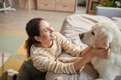 High angle portrait of smiling young woman cuddling with pet dog in cozy home interior, copy space