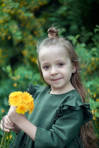 A girl blows on a bouquet of dandelions in nature in summer. Happy baby with dandelion wreath on his head with blowball having fun. Selective focus.