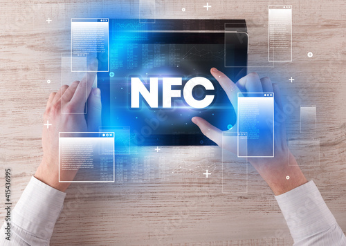 Close-up of a hand holding tablet with NFC abbreviation, modern technology concept