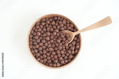 Chocolate corn balls in a wooden bowl and spoon on a white background. Top view. Copy, empty space for text