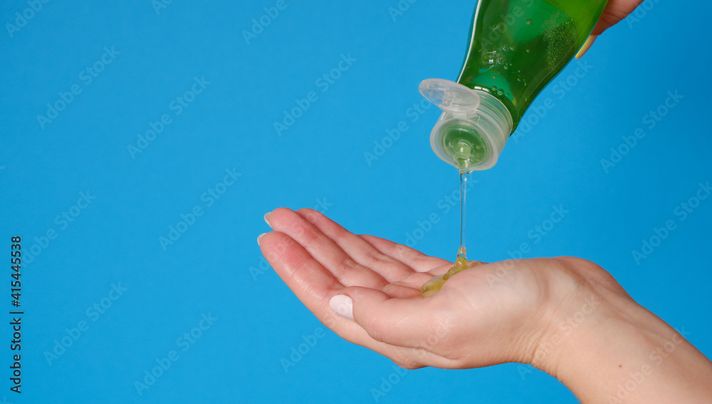Cosmetology. A woman applies shower gel to her hand. Green bottle blue background. Close up view.