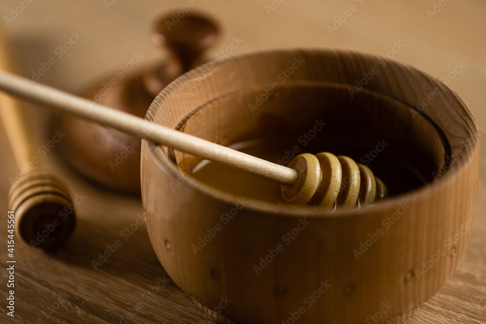 honey in a deep wooden bowl, rustic wooden plate. The wooden spoon drips slowly. honey in a deep wooden bowl, rustic wooden plate. The wooden spoon drips slowly.