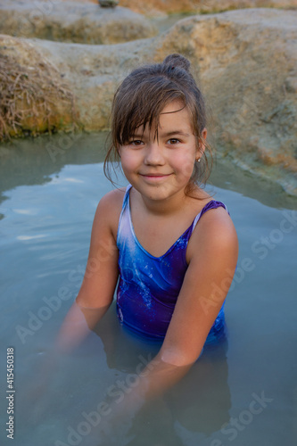 A child sits in a wild hot mineral lake in the open air and play with a mud. outdoor activities in the mountains