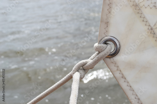 Fotografi Detail of the silver metal ring (eyelet) in a white sail, with a white knotted r