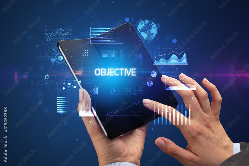Businessman holding a foldable smartphone with OBJECTIVE inscription, successful business concept Businessman holding a foldable smartphone with OBJECTIVE inscription, successful business concept