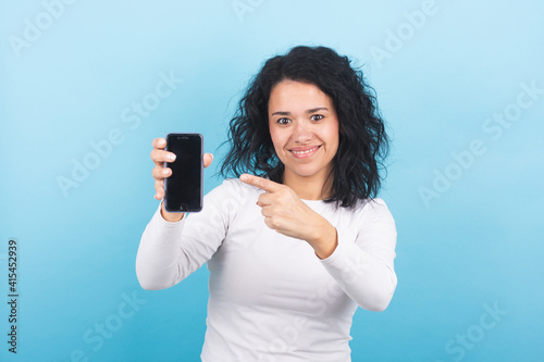 smiling brunette girl points with her finger at her mobile phone screen