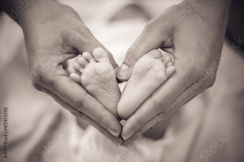 Newborn baby feet in its mother's hands shaped like a heart. Mother showing her love and affection. Monochrome