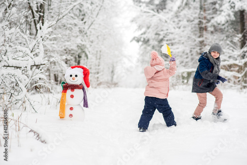 Cute boy and girl building snowman in winter forest