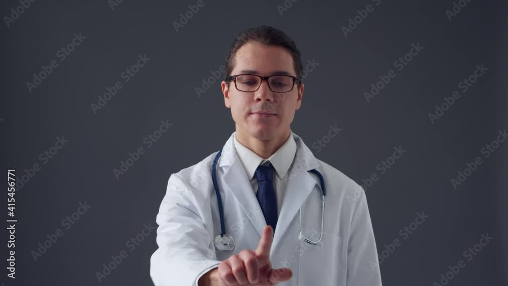 Studio portrait of young professional medical doctor working with invisible imagery digital interfaces over grey background Studio portrait of young professional medical doctor working with invisible imagery digital interfaces over grey background