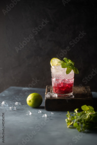 Refreshing cocktail with berry syrup or liqueur,tonic,crushed ice,fresh mint and lime on dark background.Copy space.