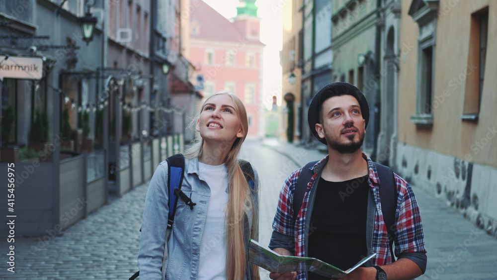 Obraz premium Happy couple of tourists with map walking on central street of old European city. They looking around and smiling.