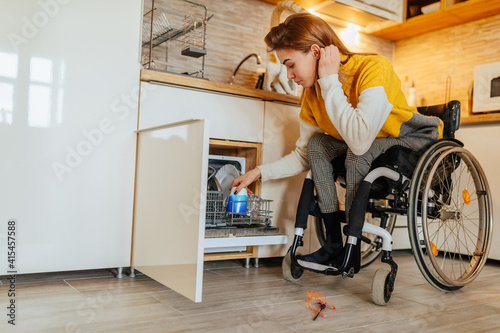 Obraz na plátne Woman in wheelchair using dishwasher