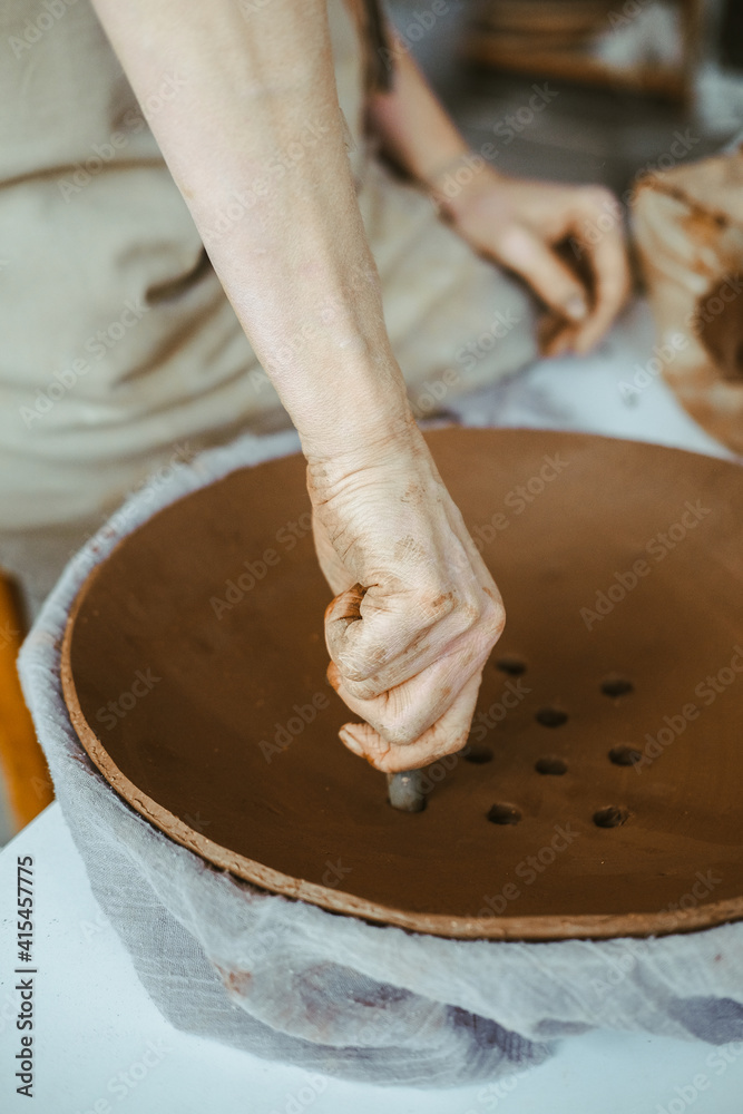 A woman's hands work with clay. Dirty fingers create a plate