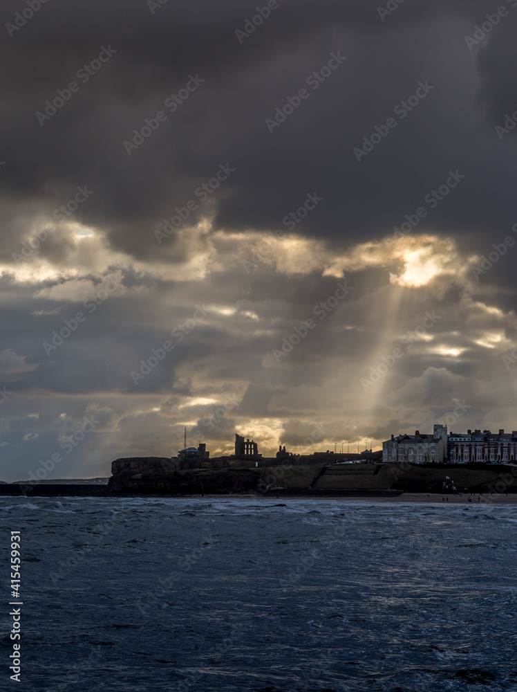 Crepuscular rays shine down on Tynemouth, the Priory & the pier in the northeast of England on a cloudy day