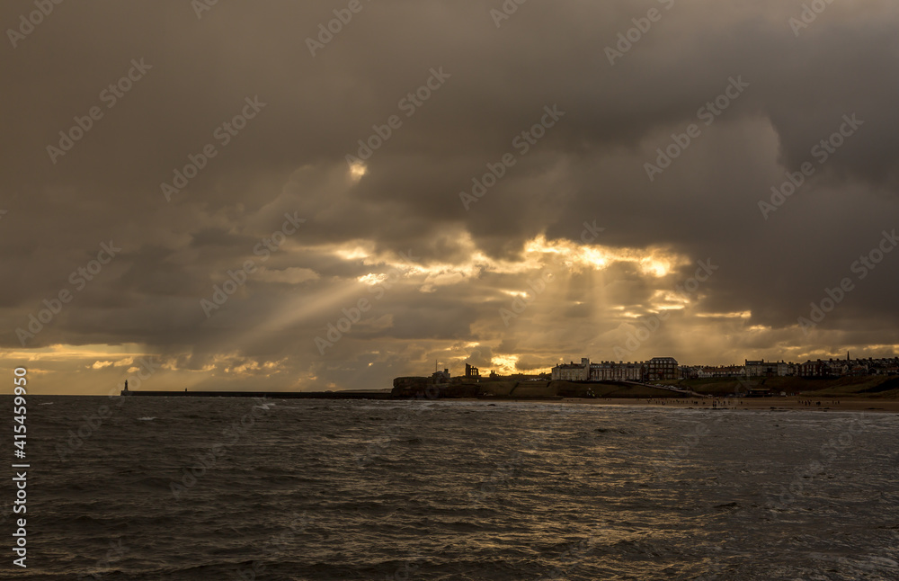 Crepuscular rays shine down on Tynemouth, the Priory & the pier in the northeast of England on a cloudy day