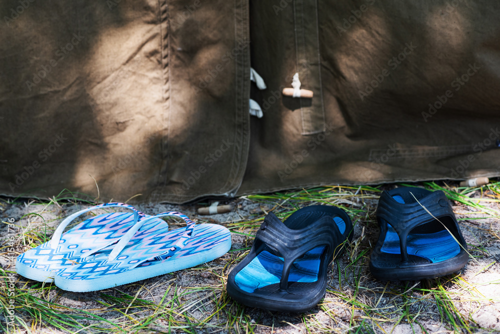 Two pairs of women's and men's summer beach slippers near tourist tent in forest. Family trip, romance concept. Selective focus.