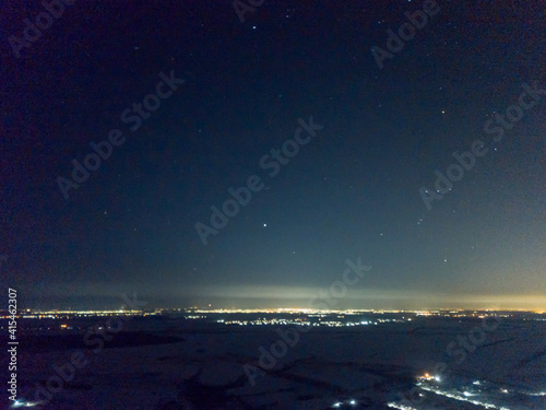 Distant lights of the night city under the starry sky. Aerial drone view. Winter frosty night. © Sergey