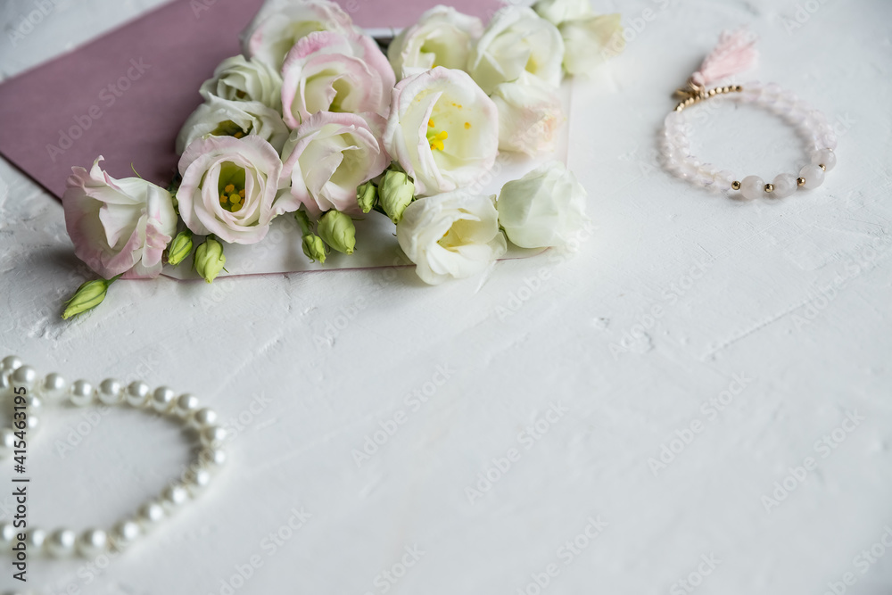 Luxury romantic background: white flowers, pearls necklace, perfume, greeting card on white.accessories and flowers. Online shopping or dating concept with copy space.