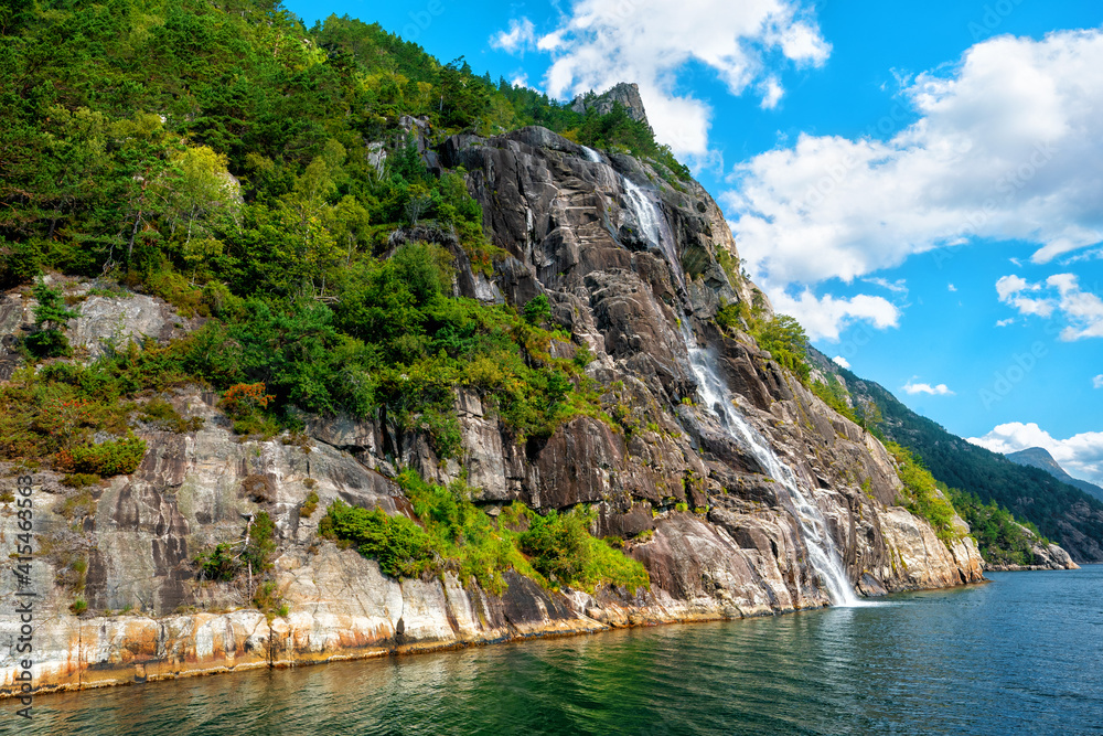 Norway Lysefjord. Rocky coast fjord teeming with cracks and waterfalls. Sunny day. Norway Lysefjord. Rocky coast fjord teeming with cracks and waterfalls. Sunny day.