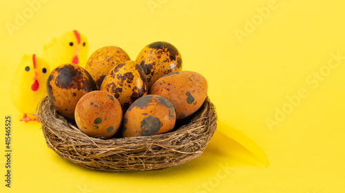 Easter quail eggs in a nest and toy chicks on a yellow background. Easter holiday concept. Close up, copy space, selective focus