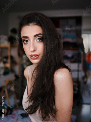 Lifestyle closeup natural light portrait of young pretty thoughtful brunette woman in shoulder straps blouse room domestic background