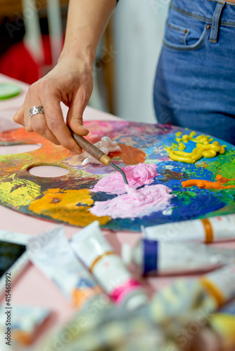 Female artist hands stirring paint on palette tubes