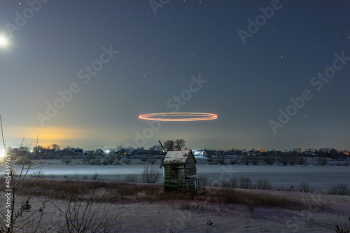 Colored lines over an old mill in a snowy field at night. Starry sky. Light graffiti