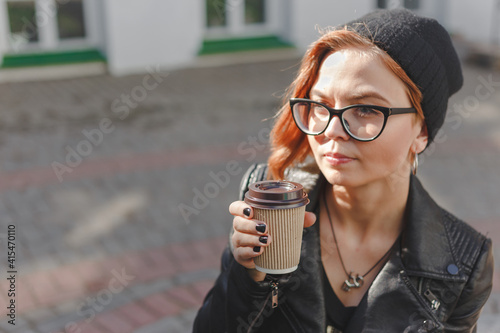 Hipster woman drinking morning coffee in sunshine light. Lifestyle portrait, girl in leather jacket, knitted hat and eyeglasses