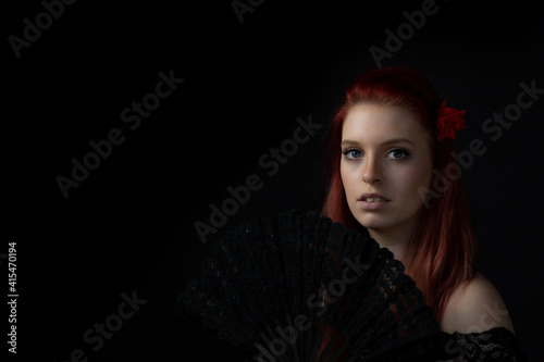 Low key portrait of beautiful young woman with fan looking at the camera. Horizontally. 