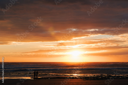 Silhouettes of two unrecognizable people on the beach enjoying a beautiful sunset