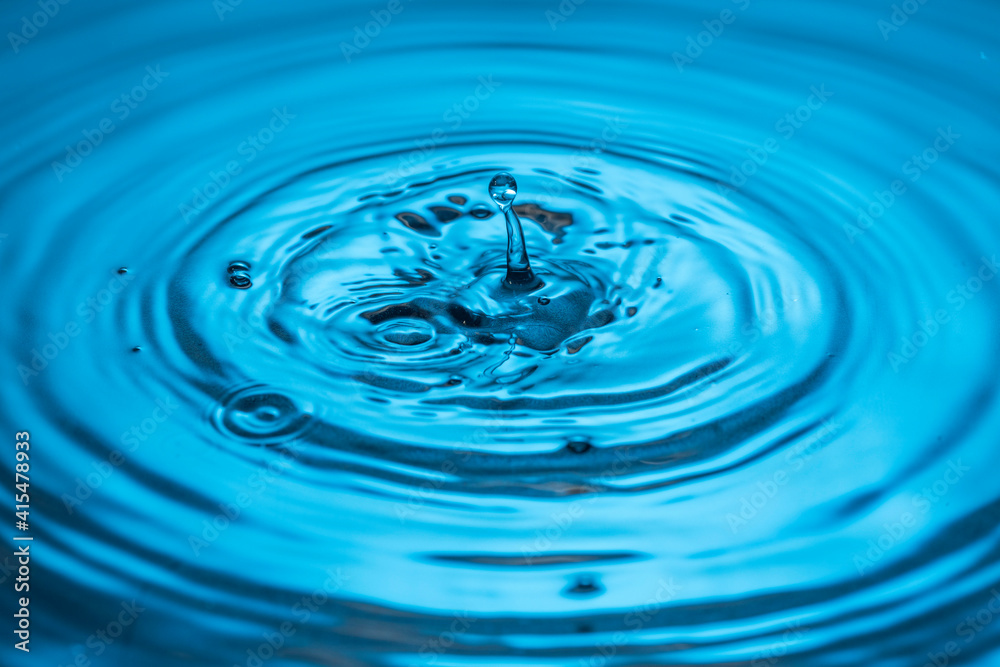 Close up view of Drops making circles on blue water surface isolated on background.