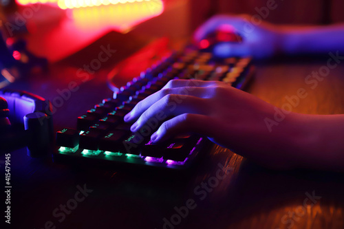 man's hands typing. A player's hands on a keyboard. The background is illuminated with led lights.