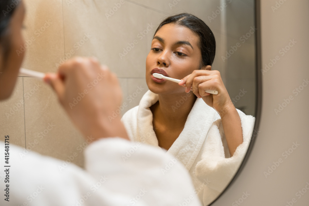 Woman wearing white bathrobe brushing her teeth Woman wearing white bathrobe brushing her teeth