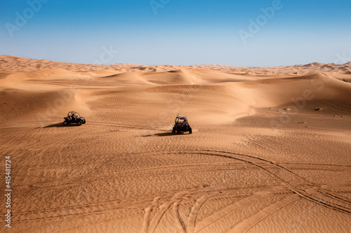 Fototapeta Naklejka Na Ścianę i Meble -  Beautiful landscape of arabic desert sand dunes with two riding quad buggy bikes, hills and wheel tracks during safari outdoor day 