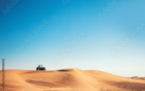 Minimalistic desert view with blue sky, sand hill and one buggy quad bike, motor sport adventures, driving off-road  