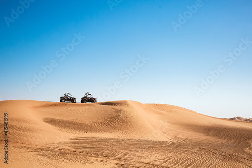 Silhouettes of two buggy quad bikes up on sand hill at blue sky background, safari tour motor vehicles for extreme sports