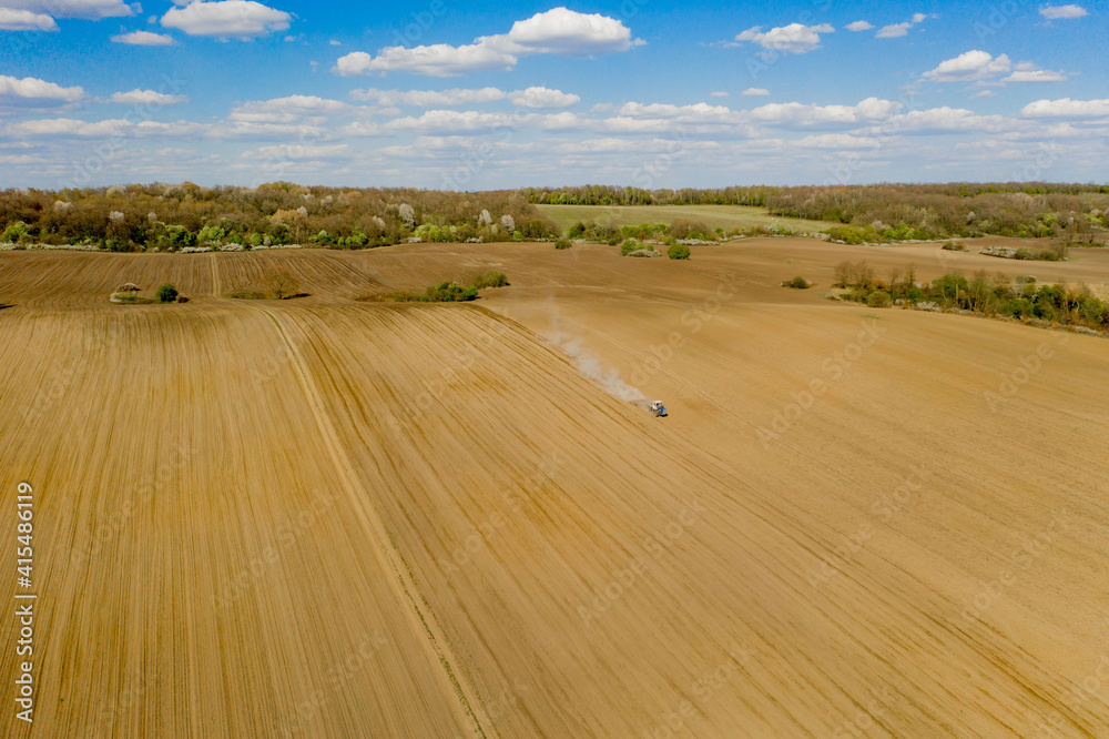Obraz premium Aerial view large tractor cultivating a dry field. Top down aerial view tractor cultivating ground and seeding a dry field. Aerial tractor cuts furrows in farm field for sowing